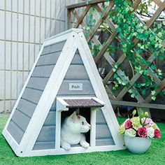 a white cat sitting in a dog house next to a potted plant on the grass