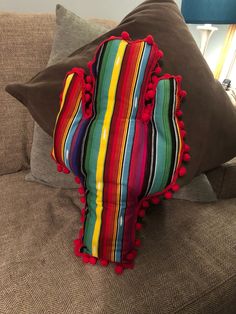 a striped pillow with pom - poms on it sitting on a couch next to a lamp