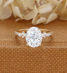 an oval cut diamond ring with three side stones on the band, sitting next to white flowers