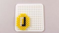 a yellow and black beaded brooch sitting on top of a white board with holes in it