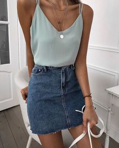 a woman sitting on a white chair wearing a blue jean skirt and grey tank top