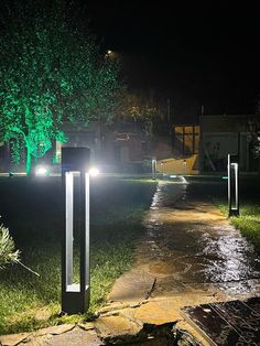 the lights are shining on the path in the park at night with green trees and grass