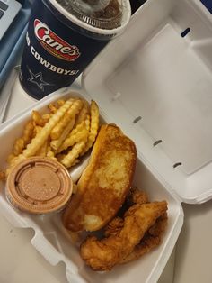 a lunch box with chicken, french fries and coleslaw on it next to a drink