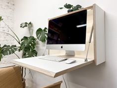 an apple computer sitting on top of a white desk next to a green potted plant