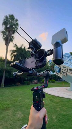 a person holding a camera in front of a boat on the grass with palm trees