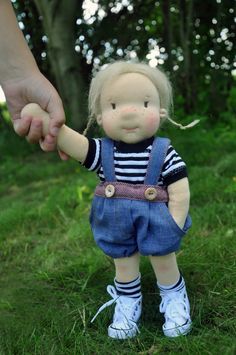 a small doll is holding the hand of a person in overalls and striped shirt