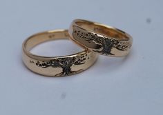 two gold wedding rings with tree designs on the sides, set against a white background