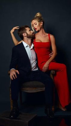 a man sitting next to a woman in a red dress on top of a chair