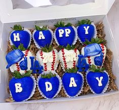 a box filled with cupcakes shaped like baseball gear and strawberries in the shape of happy birthday