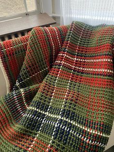 a crocheted blanket sitting on top of a couch next to a window