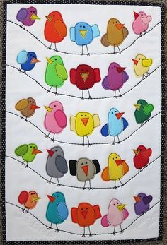 a quilted wall hanging with colorful birds sitting on a wire and looking at each other