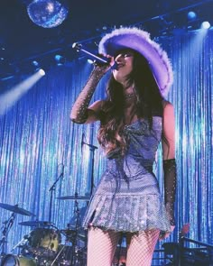 a woman wearing a purple hat and holding a microphone in front of a stage with lights