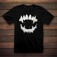 Unleash your inner nocturnal elegance with our Vampire Fangs T-shirt. Embrace the dark allure of the night with this edgy design featuring distressed vampire fangs that add a touch of mystery and rebellion. Perfect for those who have a taste for gothic fashion and a penchant for the supernatural. Elevate your wardrobe with this uniquely distressed tee that bites back. Product Features: 100% cotton (fiber content may vary for different coulors) Medium fabric (5.3 oz/yd² (180 g/m Classic fit Tear-away label Runs true to size Washing care instructions: Following these instructions will Keep the black more vivid and help avoid fading, cracking and shrinking of the garment. WASH: Printed apparel should be machine-washed cold, inside-out on a gentle cycle with a mild detergent. DRY: Printed appa Edgy Halloween T-shirt With Screen Print, Gothic Black T-shirt For Halloween, White Gothic T-shirt For Streetwear, Gothic Short Sleeve T-shirt For Halloween, Black Halloween Concert T-shirt, Edgy Halloween Concert T-shirt, Alternative Halloween Graphic T-shirt, Black Horror Tops With Skull Print, Gothic Halloween Concert T-shirt