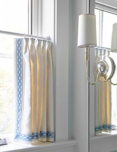 a white lamp is next to a window with blue and white curtains on the windowsill