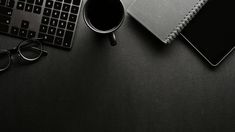 a desk with a keyboard, notebook and eyeglasses on it next to a cup of coffee