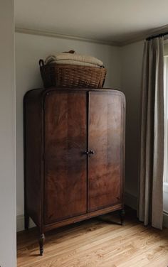 a wooden cabinet sitting in the corner of a room with a basket on top of it