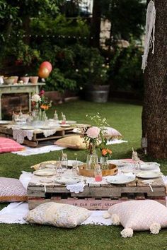 an outdoor picnic is set up in the grass with pillows and plates on it,