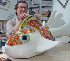 a woman sitting at a table working on a ceramic fish sculpture with colorful circles around it