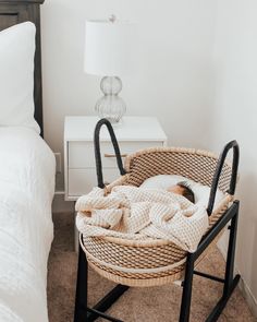 a cat laying in a basket on top of a bed next to a night stand