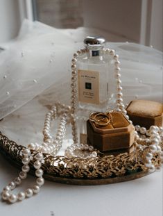 a white wedding dress with pearls and jewelry on the table next to it is a bottle of perfume