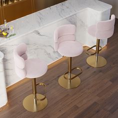 three pink velvet bar stools in front of a white marble counter with gold legs