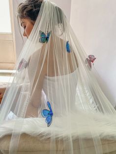 a woman sitting on top of a bed wearing a white dress and blue butterflies in her veil