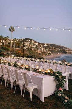 a long table is set up with candles and flowers for an outdoor dinner by the ocean