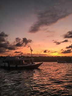 a boat floating on top of a body of water under a cloudy sky at sunset