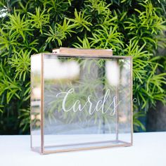 a clear box with the word cards written in cursive writing is sitting on a table