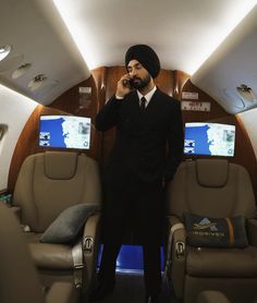 a man in a turban standing on an airplane talking on his cell phone