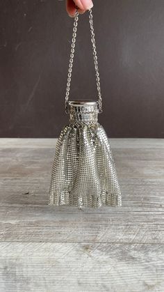 a hand is holding a silver purse on a wooden table with a chain attached to it