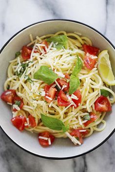 a white bowl filled with pasta, tomatoes and basil on top of a marble table