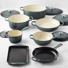 an assortment of pots and pans on a white counter top with one empty skillet in the middle