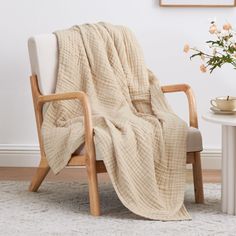 a chair with a blanket draped over it next to a table and flower vase on the floor