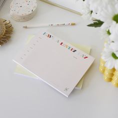 a notepad sitting on top of a white table next to flowers and pencils