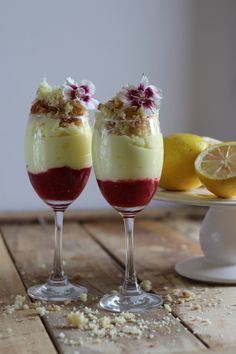 two glasses filled with dessert sitting on top of a wooden table next to lemons