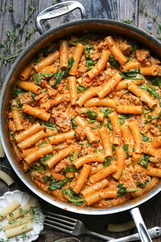 pasta with meat and spinach in a skillet on a wooden table next to utensils