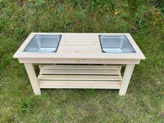 a wooden table with two bowls on it in the middle of some grass and bushes