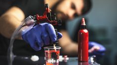 a person in blue gloves is pouring liquid into a glass with a red sprayer