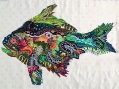 a colorful fish made out of fabric on a white sheet with floral designs and feathers