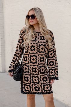 a blonde woman wearing sunglasses and a black dress is standing in front of a white brick wall