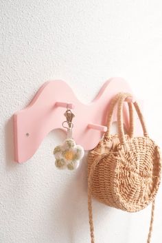 a purse hanging on the wall next to a pink coat rack with hooks and a flower