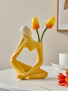 a yellow statue sitting on top of a white table next to orange and red flowers