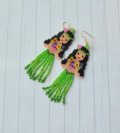 a pair of green beaded earrings featuring a woman's face with long hair