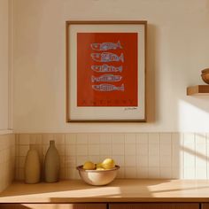 a bowl of lemons sits on a counter in front of a framed art piece