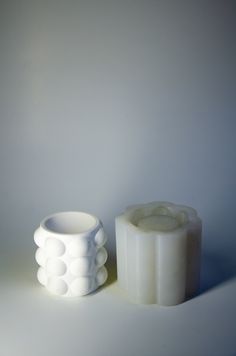 two white vases sitting next to each other on top of a table in front of a white wall