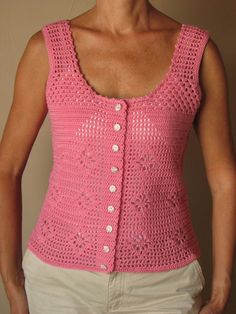 a woman wearing a pink crocheted vest and white pants with her hands in her pockets