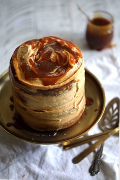 a stack of pancakes covered in caramel sauce on a gold plate with spoons