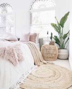 a bed with pillows and blankets in a bedroom next to two potted plants on the floor