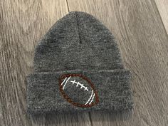 a gray beanie with a football embroidered on it sitting on top of a wooden floor